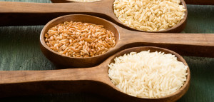 Four wooden spoons holding different types of rice